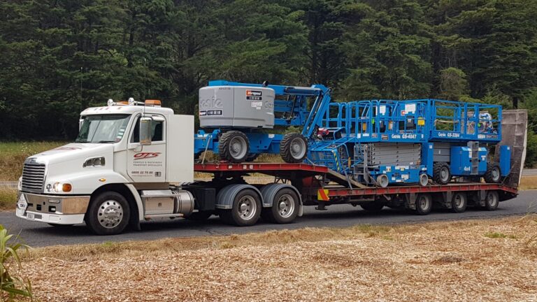 truck transporting 3 large machines with rural background